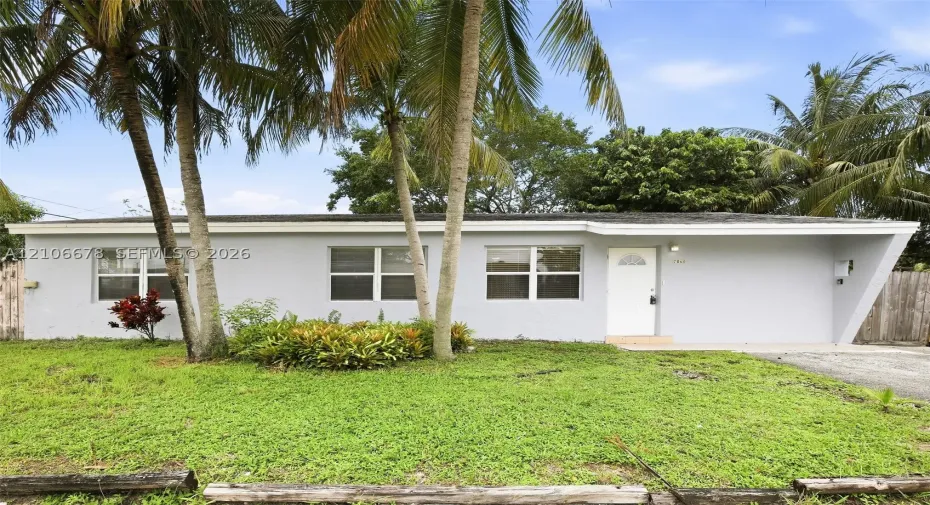 Single-story exterior featuring light-colored stucco siding, a low-slope roofline with a distinctive angled support pillar, and palm-lined landscaping