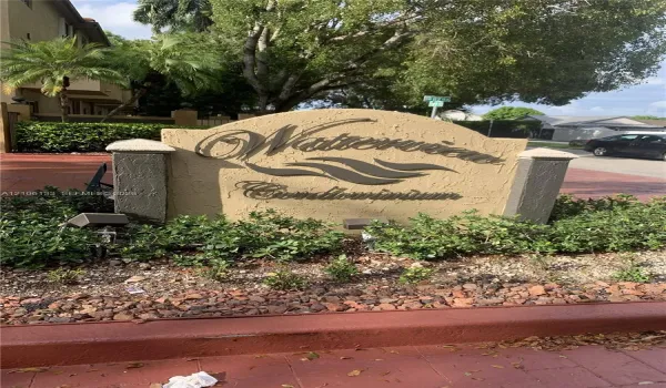 Stucco monument signage featuring metal lettering and landscape lighting, surrounded by established shrubbery and decorative stone ground cover