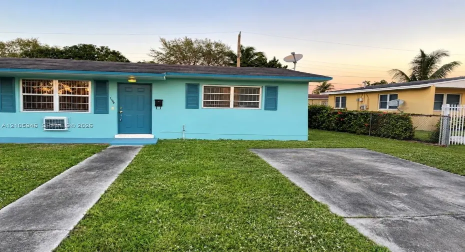 Single-story exterior featuring a vibrant painted facade, decorative window shutters, a concrete driveway, and an attached concrete walkway