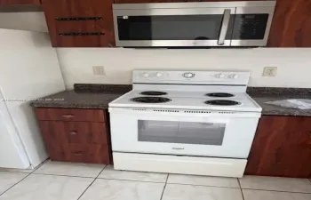 Kitchen area featuring wood-finish cabinetry, stone-texture laminate countertops, a white electric range, a stainless steel over-the-range microwave, and ceramic tile flooring