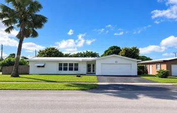 Single-story exterior featuring white stucco siding, a multi-pane grid window, double-entry glass doors, a paved driveway, and a one-car garage