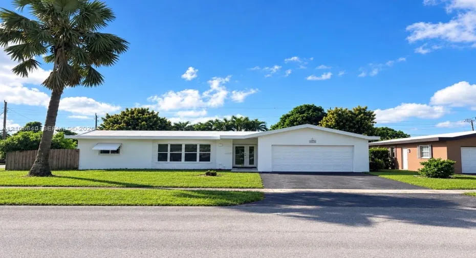 Single-story exterior featuring white stucco siding, a multi-pane grid window, double-entry glass doors, a paved driveway, and a one-car garage