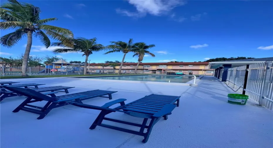 In-ground swimming pool featuring a concrete deck and metal perimeter fencing, accented by mature palm trees