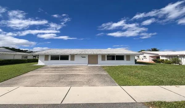 Single-story exterior featuring a white painted brick facade, concrete tile roof, shuttered windows, and a dedicated concrete driveway