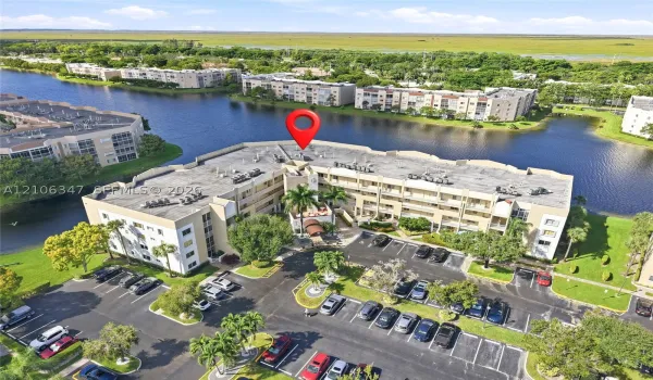 Aerial perspective featuring multi-story residential buildings, water frontage, landscaped grounds with mature palm trees, and dedicated asphalt parking