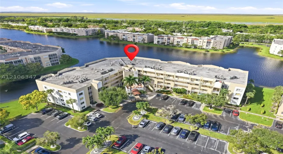 Aerial perspective featuring multi-story residential buildings, water frontage, landscaped grounds with mature palm trees, and dedicated asphalt parking