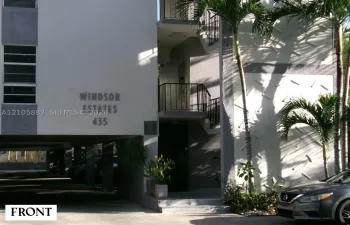 Multi-level residential exterior featuring textured stucco facade, covered ground-level parking, metal railing balconies, and mature palm landscaping