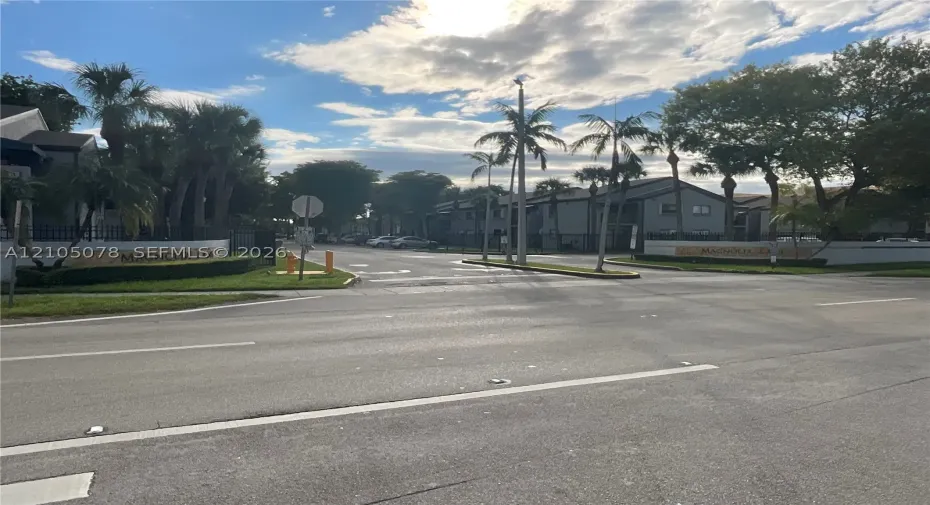 Community entrance featuring decorative stone-finish signage, mature palm trees, and manicured landscaping
