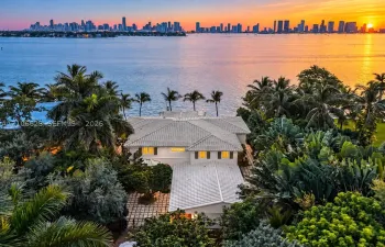 Waterfront estate featuring a tile roof, paved courtyard, lush landscaping, and a direct city skyline backdrop