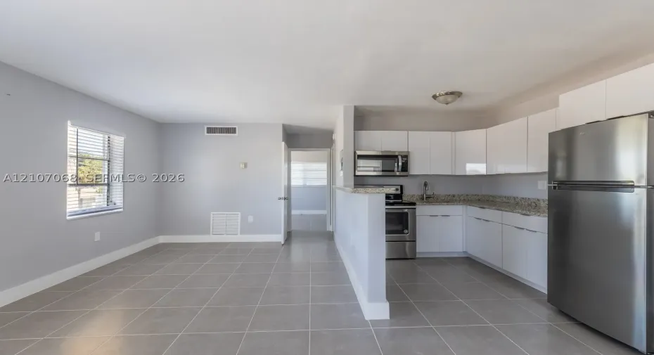 Kitchen featuring white slab cabinetry, stone-finish countertops, stainless steel appliances, and large-format tile flooring