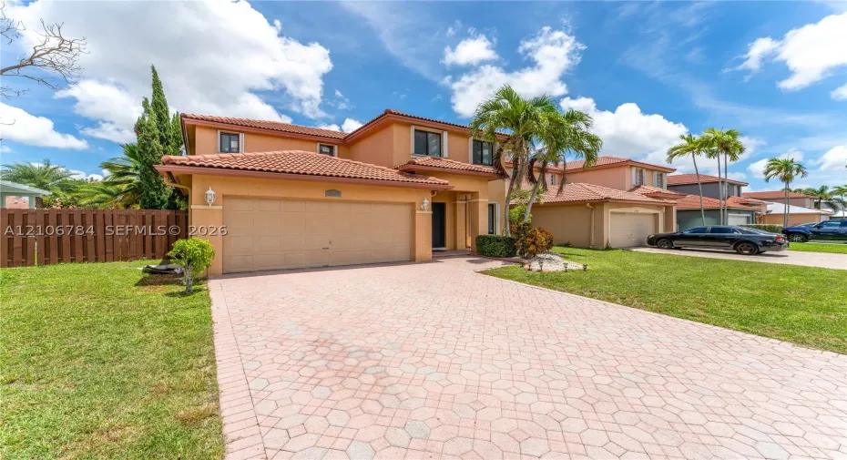 Two-story residence featuring a tile roof, stucco exterior, two-car garage, and a patterned paver driveway