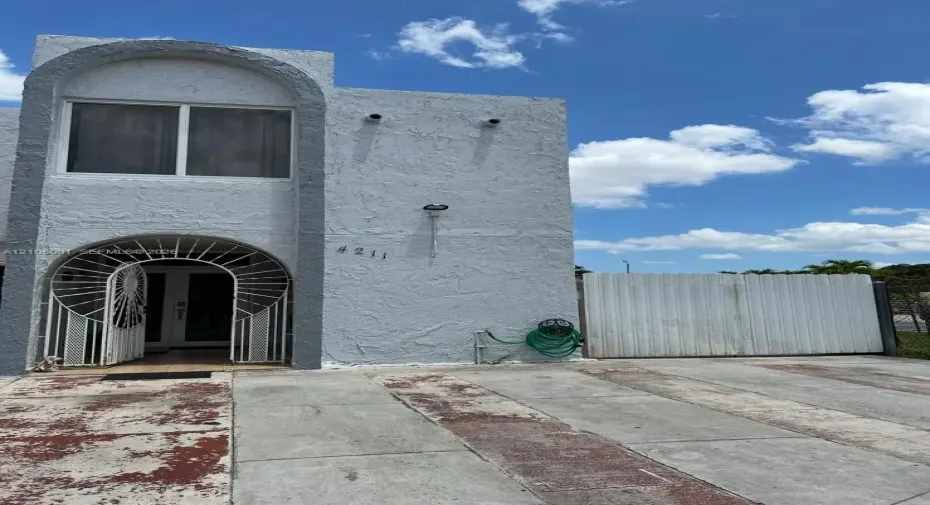 Stucco exterior featuring arched architectural details, decorative metal security gate, double-entry doors, and a private concrete driveway