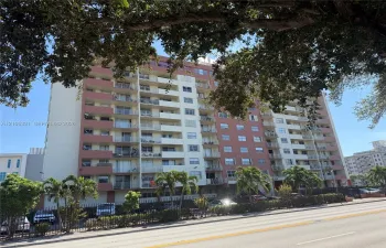 Multi-story high-rise exterior featuring individual recessed balconies, concrete construction, and perimeter fencing