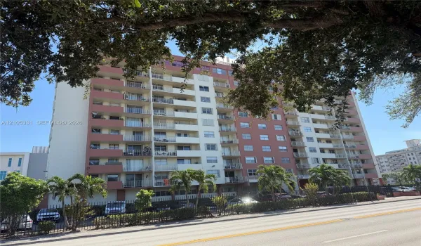 Multi-story high-rise exterior featuring individual recessed balconies, concrete construction, and perimeter fencing