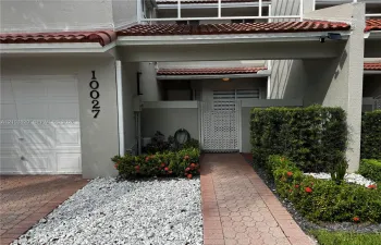 Exterior facade featuring a stucco finish, red tile roofing, paved walkway, integrated single-car garage, and enclosed courtyard entrance