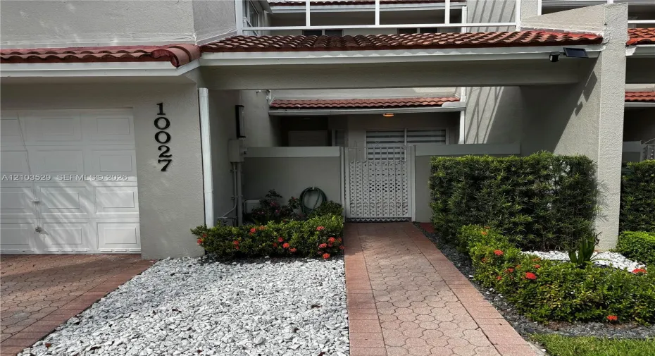 Exterior facade featuring a stucco finish, red tile roofing, paved walkway, integrated single-car garage, and enclosed courtyard entrance