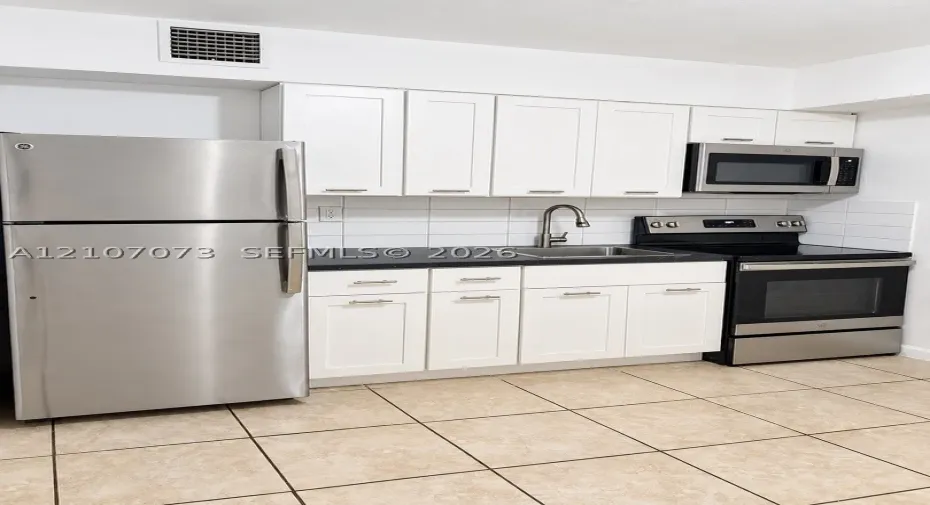 Kitchen featuring white shaker-style cabinetry, dark stone countertops, stainless steel appliances, ceramic tile flooring, and a subway tile backsplash