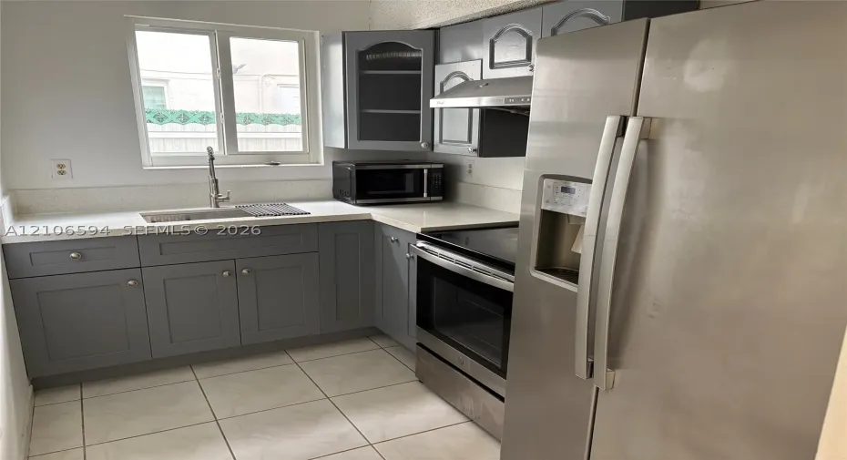 Kitchen featuring gray shaker-style cabinetry, white solid-surface countertops, stainless steel appliances, and tile flooring