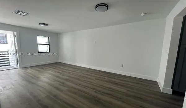 Interior space featuring wood-finish flooring, white walls, dual flush-mount ceiling light fixtures, and a single-pane window