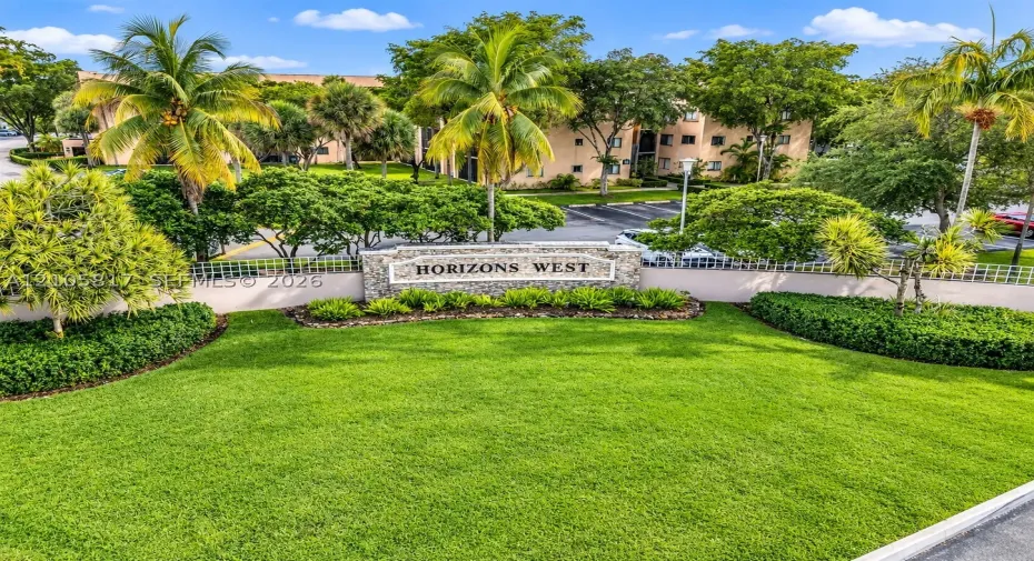 Horizons West monument sign featuring stone masonry accents, surrounding lush landscaping, mature palm trees, and manicured lawn