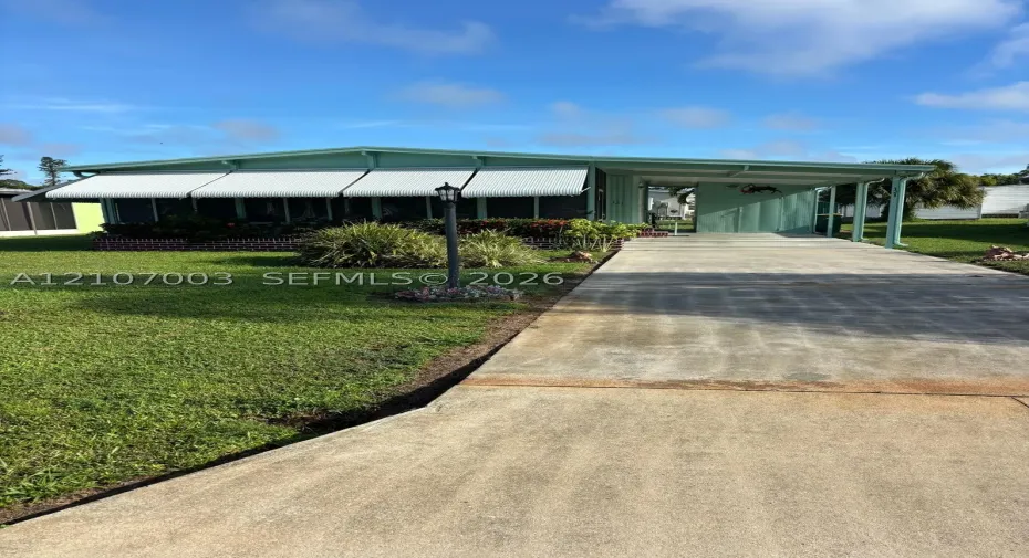 Exterior featuring a concrete driveway, attached carport, screened-in porch, metal window awnings, and a brick-bordered garden bed