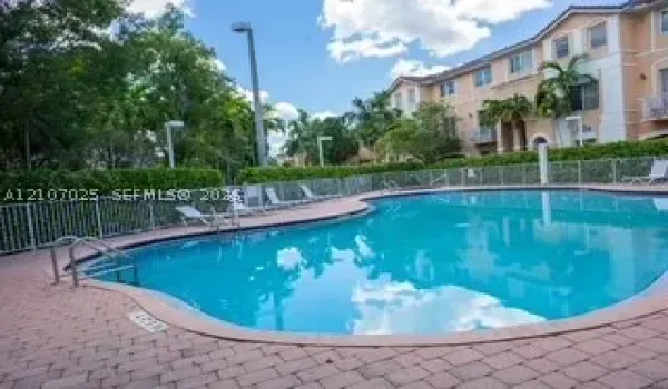 Swimming pool with a paved deck, metal perimeter fencing, and mature landscaping