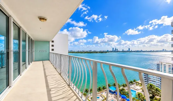 Covered balcony with a powder-coated metal railing, full-height sliding glass doors, and panoramic water and city skyline surroundings