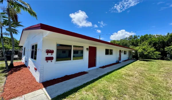 Single-story exterior featuring white stucco siding, a low-pitched roof with red eaves, a concrete walkway, and red entry doors
