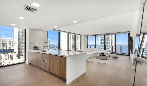 Kitchen featuring a center island with light-toned stone-finish countertop, wood-finish cabinetry, under-mount sink, and recessed lighting throughout, complemented by wood-finish flooring and expansive floor-to-ceiling windows