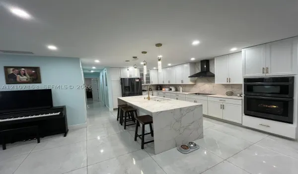 Kitchen featuring white cabinetry, waterfall-edge island with stone-finish countertop, stainless steel double wall oven, patterned stone-finish backsplash, and recessed lighting