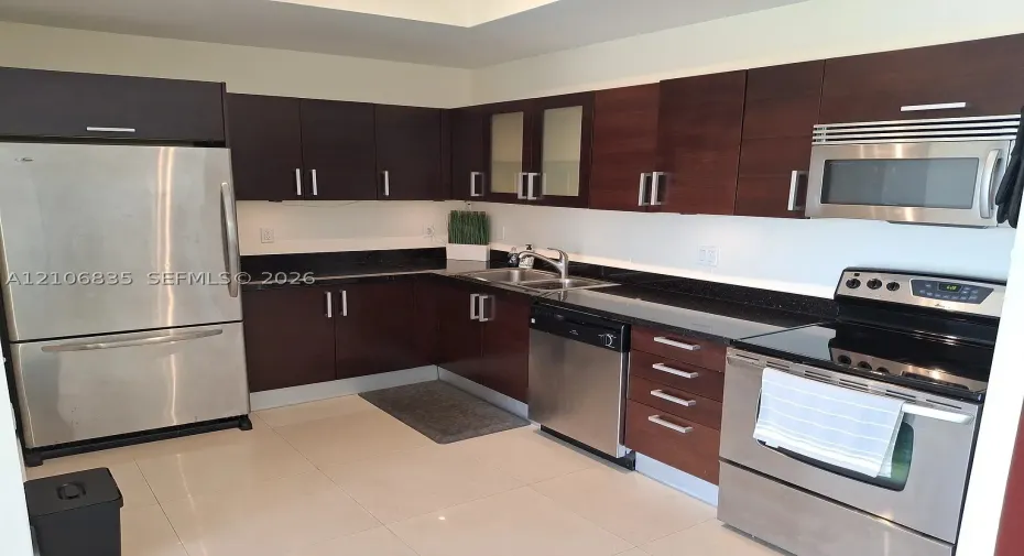 Kitchen featuring dark wood-finish cabinetry, solid surface countertops, stainless steel appliances, double-basin sink with arched faucet, and tile flooring