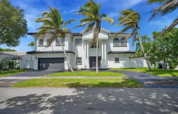 Two-story residence featuring a central portico with classical columns, stucco exterior, arched upper windows, and a paved driveway leading to an attached multi-car garage