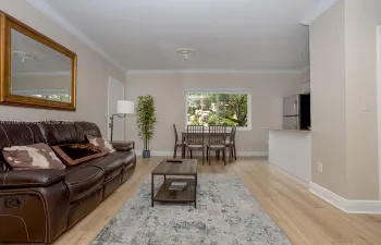 Living space featuring wood-finish flooring, neutral wall paint, crown molding, a large sliding window, and a breakfast bar with stainless steel appliances