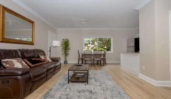 Living space featuring wood-finish flooring, neutral wall paint, crown molding, a large sliding window, and a breakfast bar with stainless steel appliances