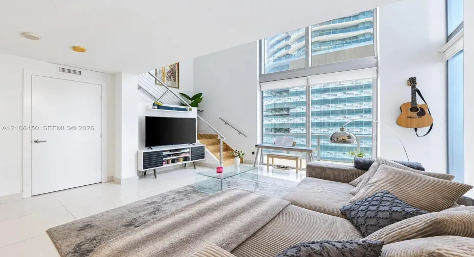 Living area featuring floor-to-ceiling windows, porcelain tile flooring, and a staircase with metal railings