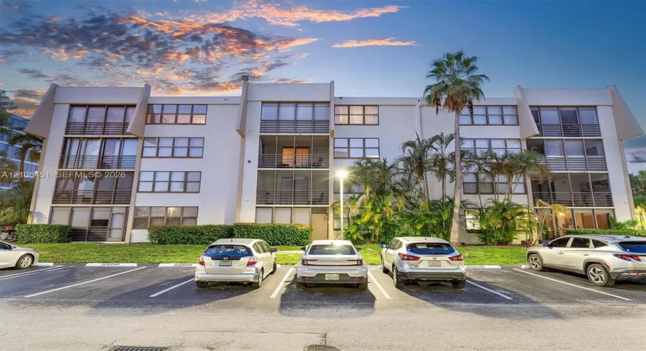 Multi-story residential building featuring a reinforced concrete facade, screened-in balconies, large grid windows, and established tropical landscaping