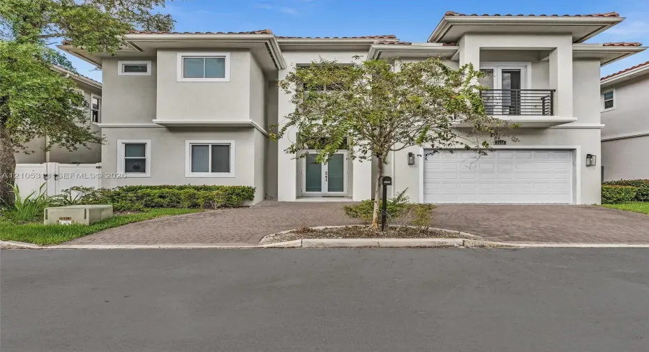 Two-story stucco exterior featuring a paved driveway, integrated two-car garage, upper-level balcony with metal railing, and double-entry doors