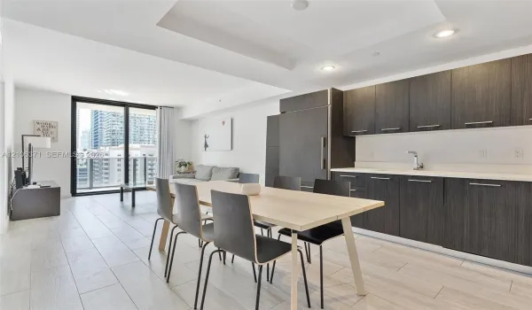 Modern kitchen featuring dark-toned cabinetry, light-toned countertops, recessed lighting, wood-finish flooring, and a glass sliding door leading to an outdoor balcony