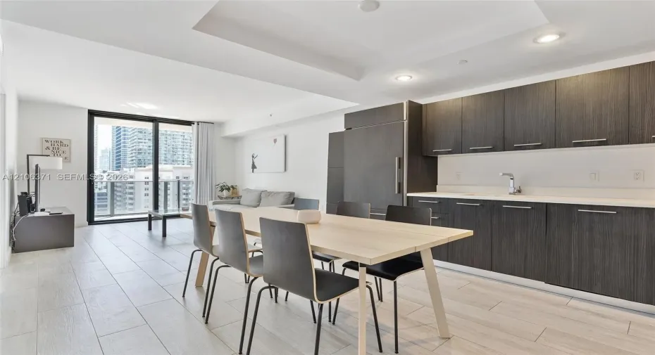 Modern kitchen featuring dark-toned cabinetry, light-toned countertops, recessed lighting, wood-finish flooring, and a glass sliding door leading to an outdoor balcony
