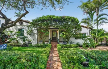 Stucco exterior residence featuring a clay tile roof, brick walkway, and landscaped garden beds