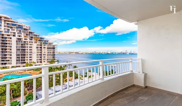 Private balcony featuring wood-finish flooring and a white powder-coated metal railing overlooking a waterfront and urban landscape