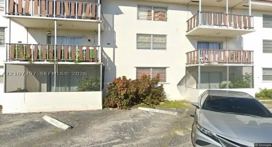 Multi-story stucco exterior featuring screened balconies, open-air upper-level balconies, and designated surface parking spaces