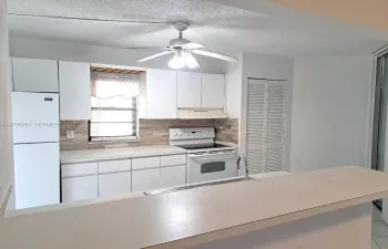 Kitchen featuring white cabinetry, stone-finish backsplash, built-in range, refrigerator, and solid surface breakfast bar