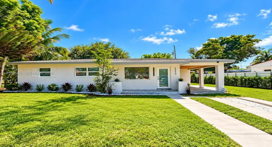 Single-story residence featuring a smooth stucco exterior, covered carport, manicured lawn, and landscape bed with ornamental plantings