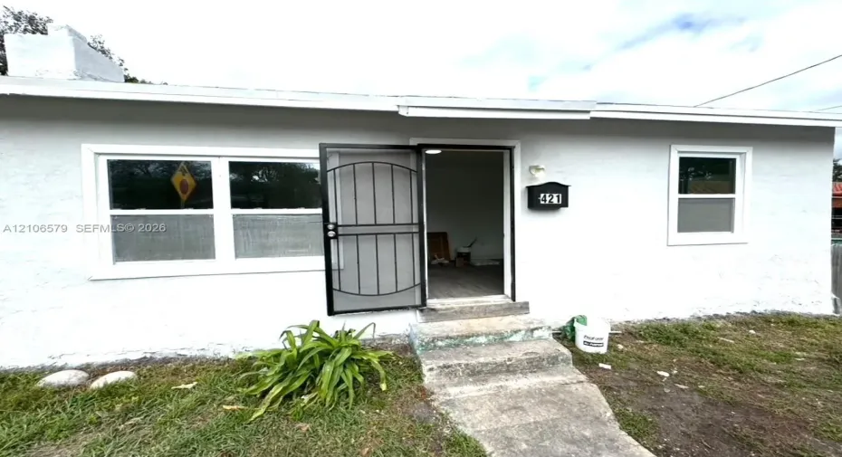 Exterior featuring a white stucco facade, metal security screen door, concrete front steps, and a wall-mounted mailbox