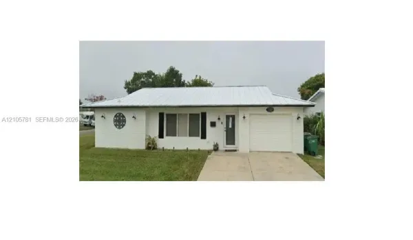 Single-story residence featuring white painted brick masonry, a standing seam metal roof, attached single-car garage, and concrete driveway