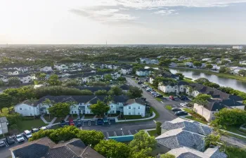 Aerial perspective of a multi-unit residential community featuring shingle-style roofing, paved parking areas, sidewalk pathways, and a water feature