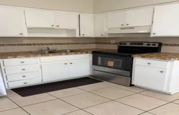Kitchen featuring white cabinetry, tiled countertops with decorative stone backsplash, stainless steel range, and ceramic tile flooring