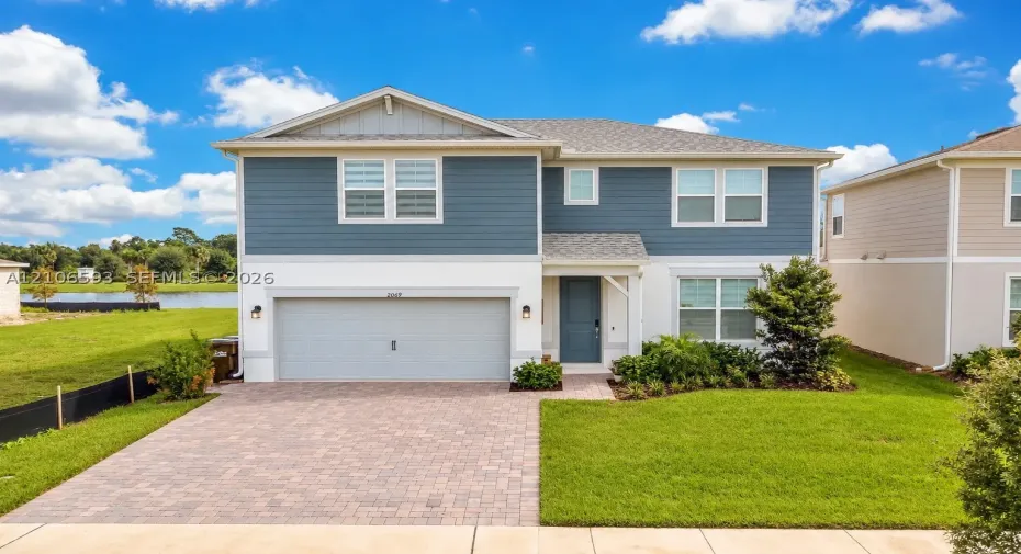 Two-story residence featuring a multi-textured exterior of lap siding and stucco, a paved driveway, a two-car garage, and a covered front entryway