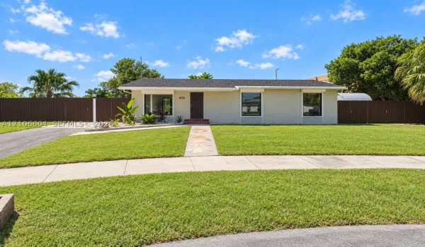 Single-story exterior featuring a neutral stucco facade, asphalt shingle roof, flagstone walkway, and full-perimeter privacy fencing